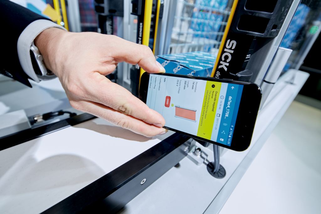 Hand holds smart phone up to deTec4 safety light curtain; smart phone shows override error using NFC
