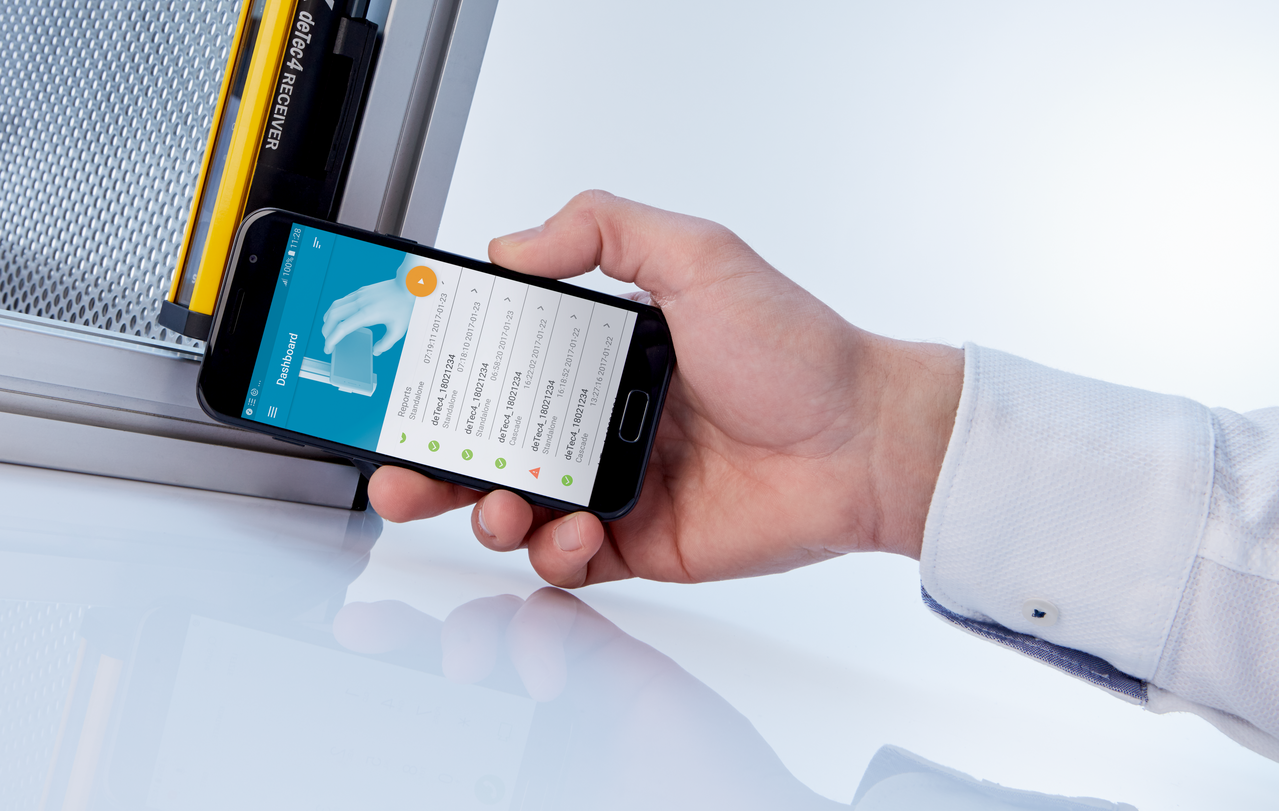 Hand holds smart phone up to deTec4 safety light curtain; smart phone shows dashboard of deTec4