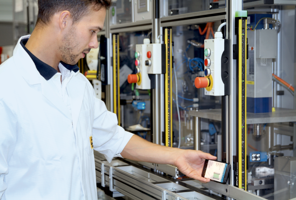 Male worker in white lab coat holds smart phone up to safety light curtain to pull reports using NFC